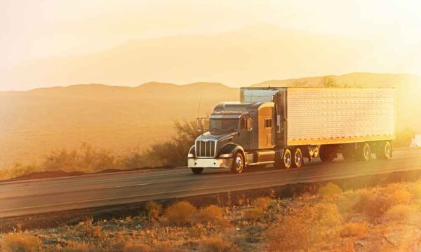 tractor trailer traveling down highway framed by a sunset