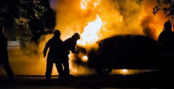 Firefighters surrounding a car in flames at night