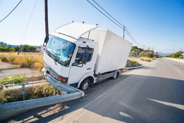 A white box truck is shown crashed into the guard rail on a highway.