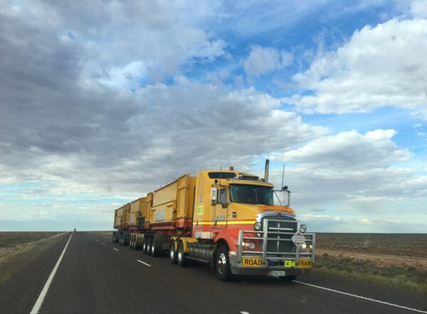 Large yellow commercial truck with multiple trailers driving on highway set against blue sky with clouds