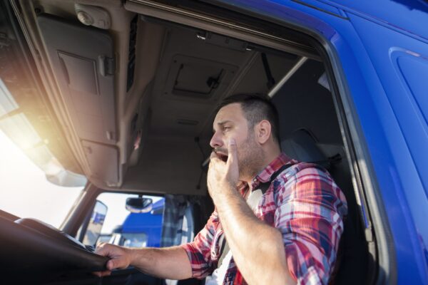 Truck driver in blue truck wearing plaid shirt and yawning