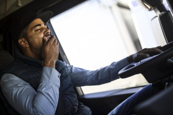 Truck driver wearing black hat and vest covering mouth while yawning