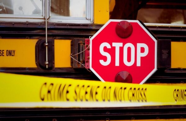 Yellow police tape in the foreground with a school bus stop sign arm extended in the background. The recent school bus crash in Tennessee has left two dead.