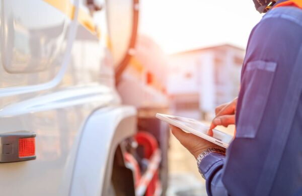 Truck driver stands in front of commercial truck with a tablet, checking off a list