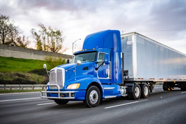 A large truck with a dark blue cab and white trailer speeding down a local highway.