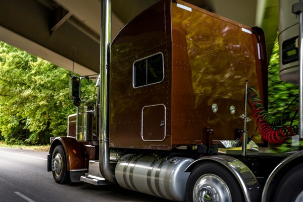 A massive brown semi truck passing under a bridge at high speeds.