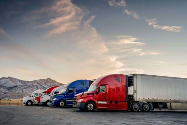 Carrier trucks lined up at a truck stop with mountains in the background.