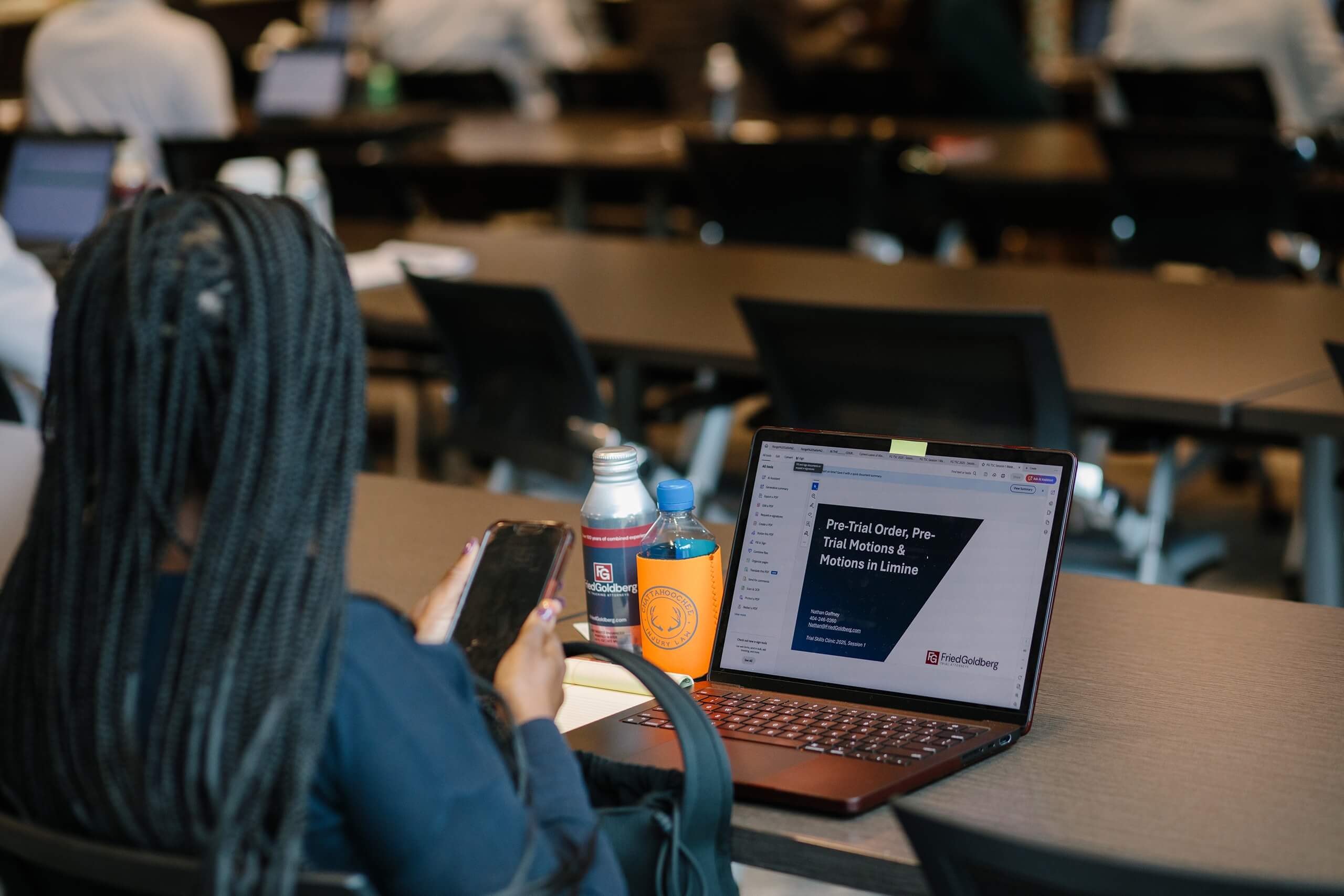 Attendee views phone and laptop showing pre-trial motions slide at Trial Skills Clinic 2025.