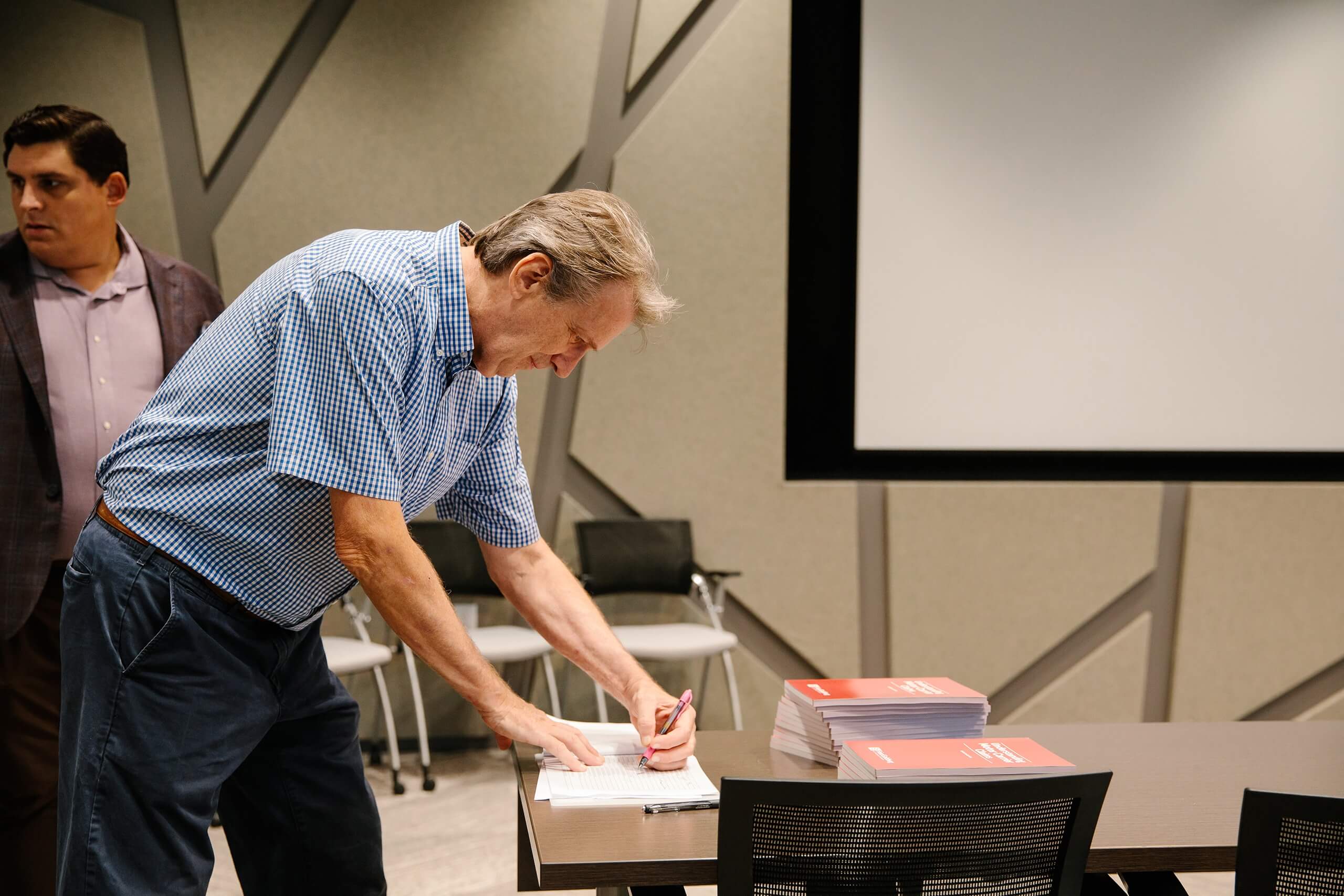 An attendee signs paperwork on a table stacked with red training booklets during the Trial Skills Clinic 2025.