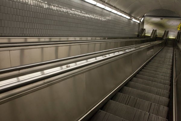 Empty underground escalator in a tiled transit station, viewed from the bottom looking up toward a curved tunnel ceiling. (469505969)
