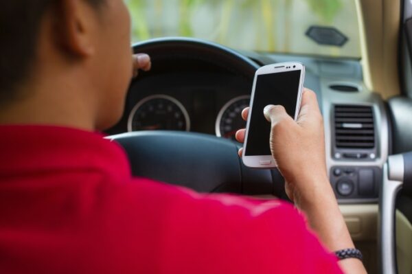 Man with red shirt texting on his cell phone while driving