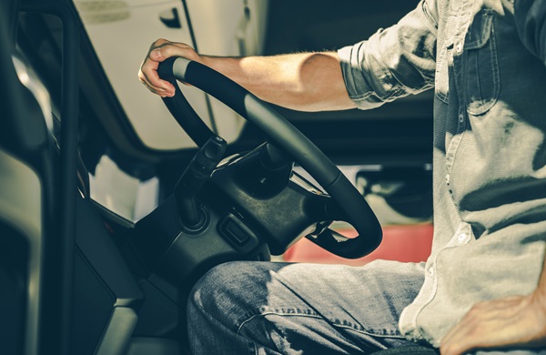 A truck driver sits in the cab with one hand on the steering wheel and the other resting on his leg. (246271677)
